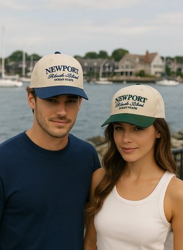 A man and woman wearing matching Newport Rhode Island caps by the waterfront.