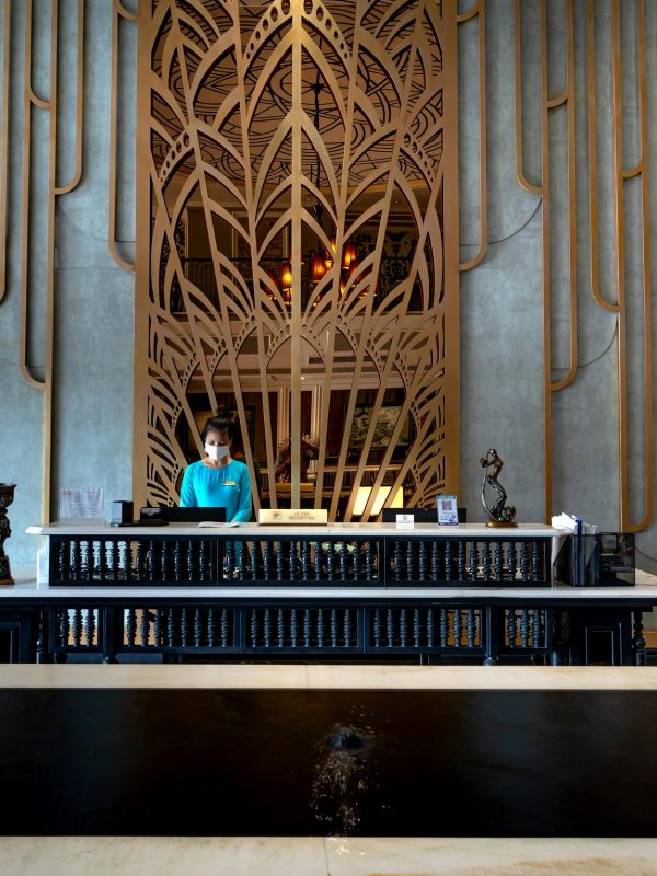 Reception desk with ornate wooden backdrop and a masked staff member in a blue uniform.