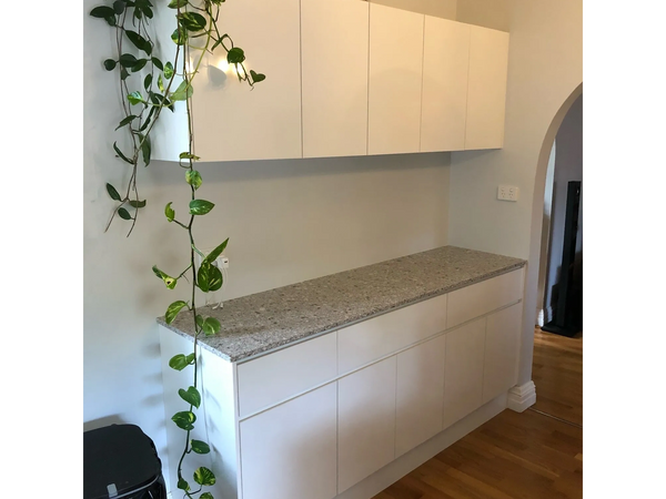 Minimalist white cabinetry with speckled stone benchtop and trailing indoor plant in hallway nook.