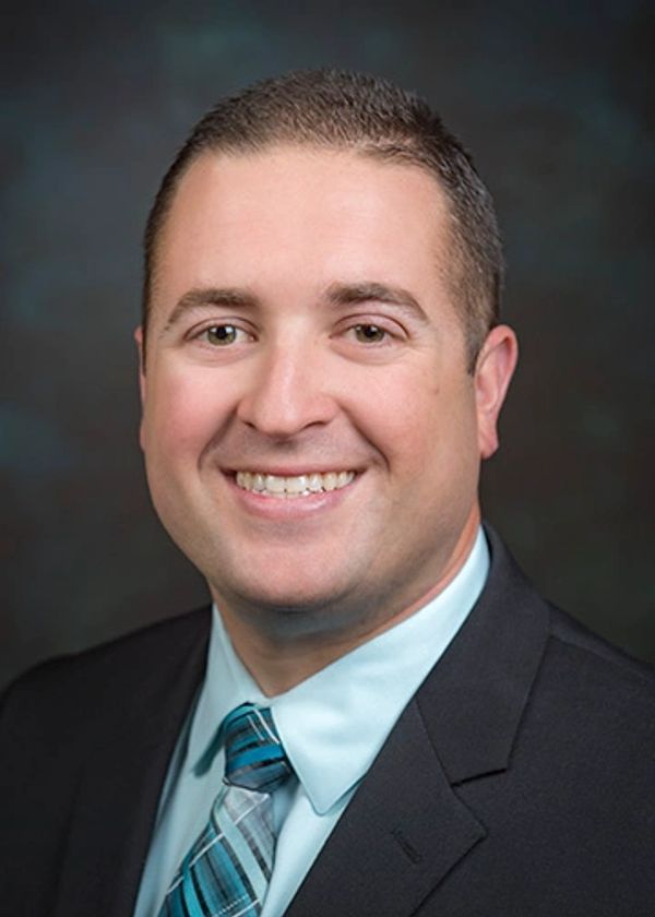 Professional man smiling in a suit and tie against a dark background.