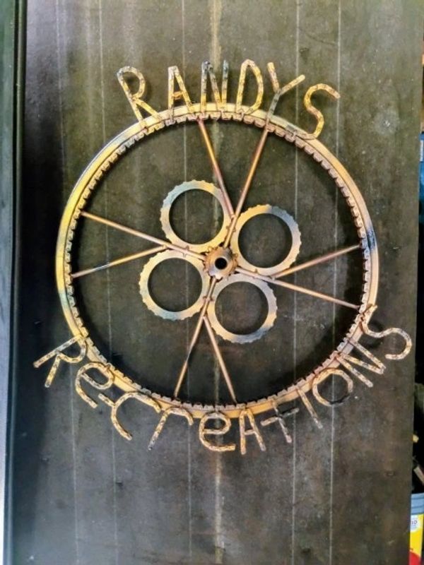 Rustic metal sign reading 'Randy's Recreations' with bike parts.