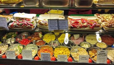 A deli display with various sandwiches, salads, and toppings.