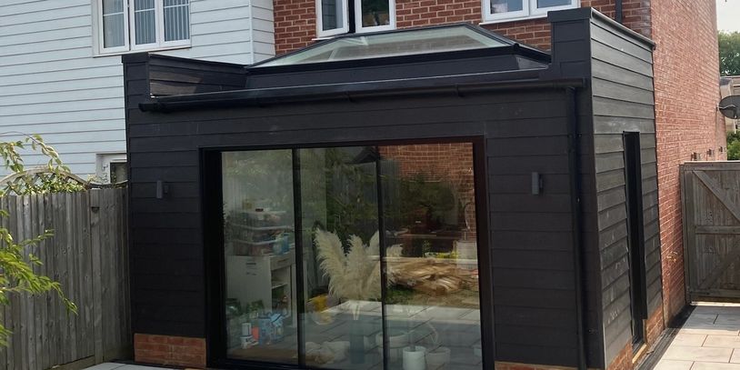 Modern black garden room extension with glass doors and skylight.