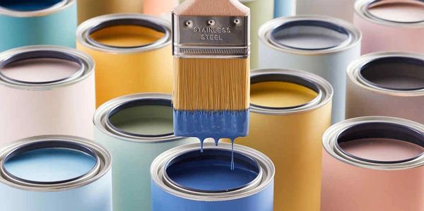 Paintbrush dripping blue paint over open colorful paint cans.