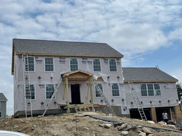 A two-story house under construction with ladders against the walls and a cloudy sky.