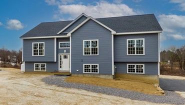 A newly built blue house with white trim and multiple windows under a clear sky.