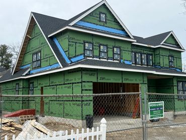 A large house under construction with green ZIP System sheathing and black roof shingles.
