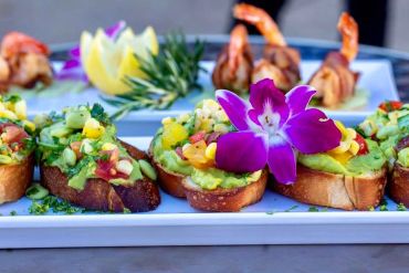 Colorful seafood appetizers with edible flowers on a white plate.