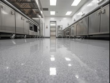 A modern commercial kitchen featuring a seamless, high-gloss epoxy floor in a neutral gray tone.