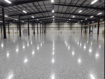 A highly polished, seamless epoxy floor in a vast, well-lit warehouse or factory setting.