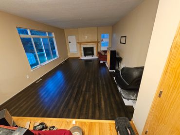 Empty living room with dark wood flooring, a fireplace, and large window.