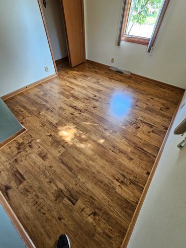 Empty room with shiny wooden flooring and a window letting in sunlight.