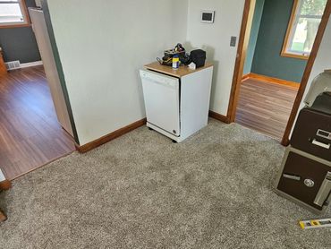 A small dishwasher with tools on top in a carpeted corner room.