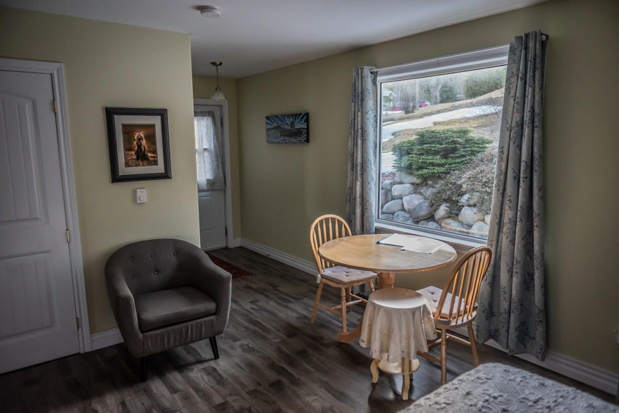 Cozy dining nook with a round table, wooden chairs, and large window showing outdoor greenery.