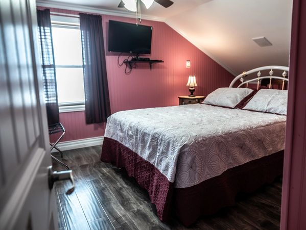 Cozy bedroom with pink walls, white bedspread, and mounted TV.