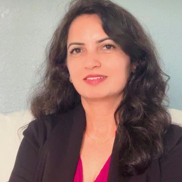 Portrait of a confident woman with long dark hair, wearing a black blazer and red top.