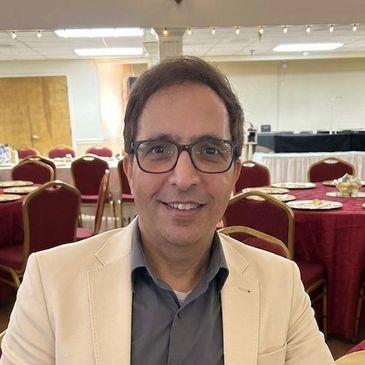 Man wearing glasses and a beige blazer smiling indoors.