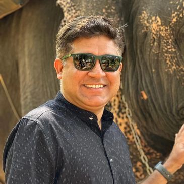 Man smiling wearing sunglasses in front of an elephant.