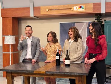 Four smiling people enjoying drinks on an NBC 10 set.