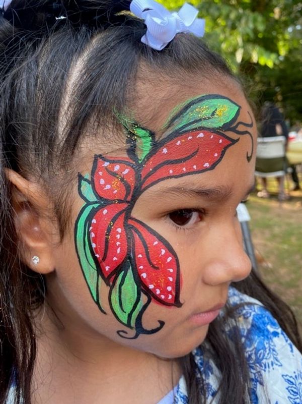 Young girl with colorful butterfly face paint at an outdoor event.