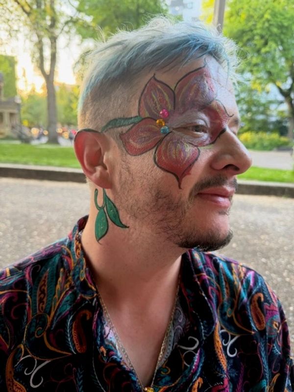 Man with blue hair and vibrant floral face paint in a colorful shirt outdoors.