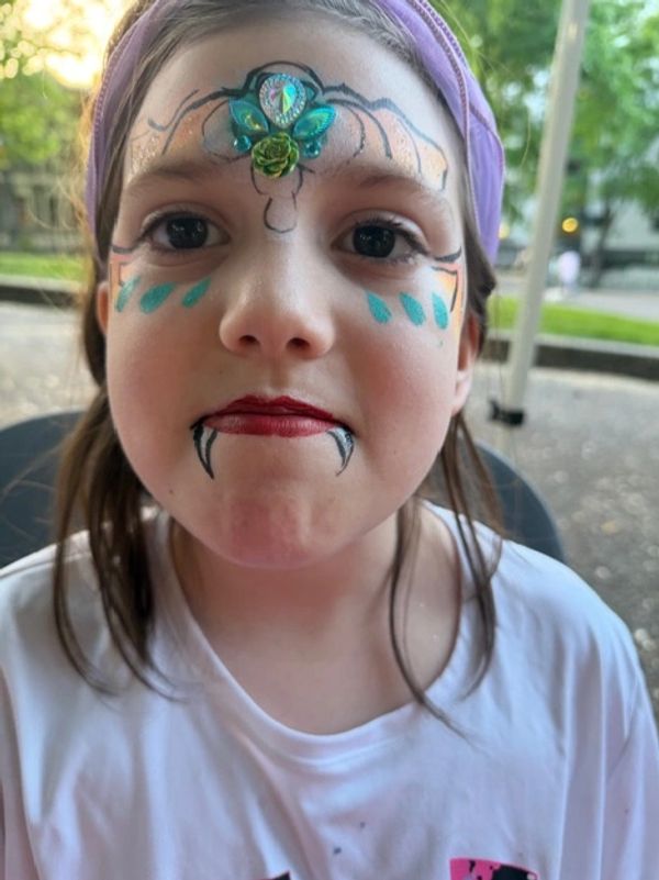 Child with face paint resembling a vampire and decorative forehead jewels.
