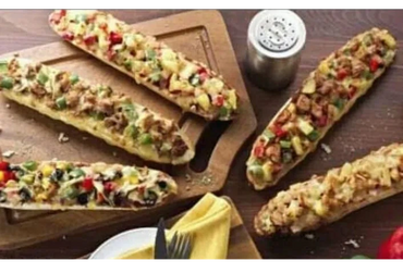Five slices of vegetable and meat-topped bread on wooden boards with salt shaker and utensils.