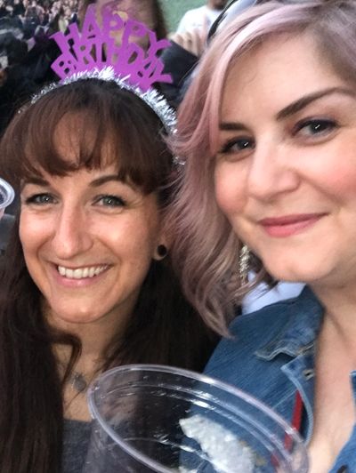 Two women smiling, one wearing a birthday headband, holding drinks.