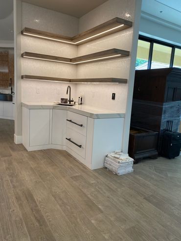 Modern kitchen corner with white cabinets, floating shelves, and wood-look flooring.
