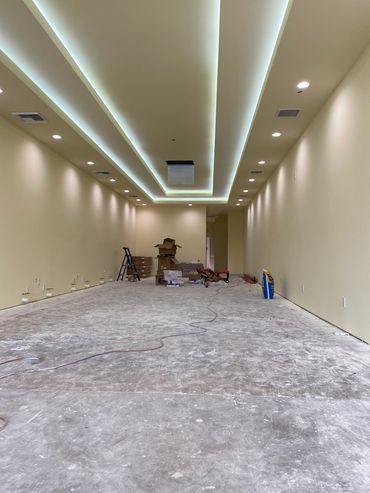 Long room under construction with recessed ceiling lights and scattered materials.