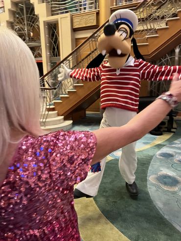 Person in pink sequined outfit reaching out to Goofy in a striped shirt inside a building.