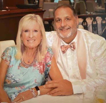 Smiling couple seated at a table, holding hands, dressed in colorful attire at a formal event.