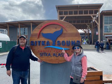Two people posing near Sitka Sound Cruise Terminal sign in Alaska.