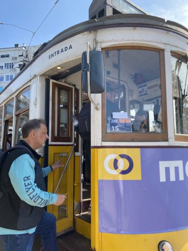 Man boarding a vintage yellow tram marked 'ENTRADA' on a sunny day.