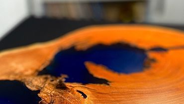 Wood slab table with blue resin river design on black surface.