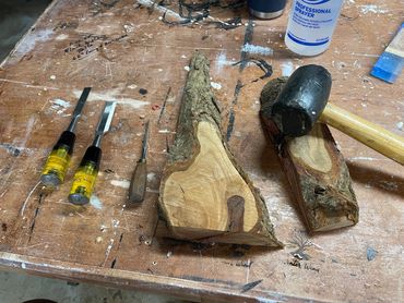 Wood carving tools and wood pieces on a workbench with a rubber mallet.