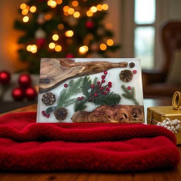 A festive resin block with pinecones, berries, and wood on a red cloth, with Christmas lights in the background.