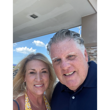 Smiling middle-aged couple outdoors under a bright sky.