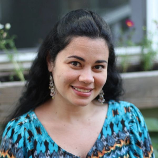 Smiling woman with dark hair and blue patterned dress outdoors.