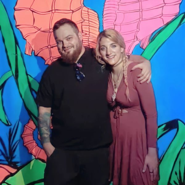 Two people smiling in front of a colorful wall.