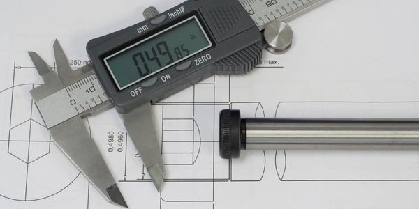 Digital caliper measuring a metal rod on a technical drawing.