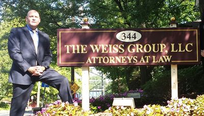 Attorney Leonard Weiss stands next to a sign reading "344 The Weiss Group LLC Attorneys at Law"