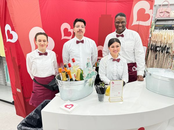 Four bartenders in white shirts and maroon bow ties at a beverage station.