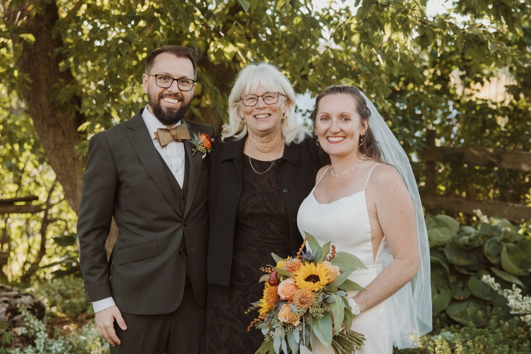 Happy bride, groom, and woman posing outdoors.