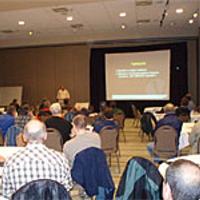 A group of people are seated at tables facing a presenter at the front of a seminar room.