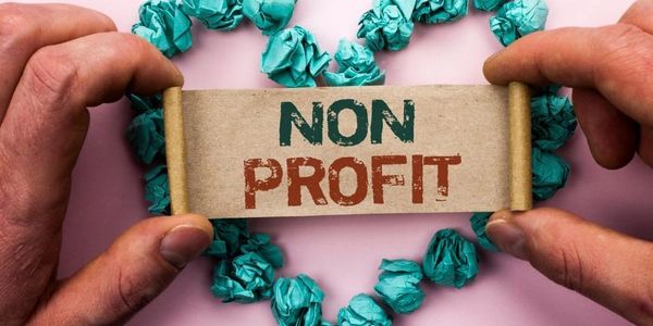 Hands holding a scroll with 'NON PROFIT' inside a heart made of crumpled blue papers.