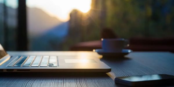 Laptop and smartphone on a wooden table with sunrise in the background.