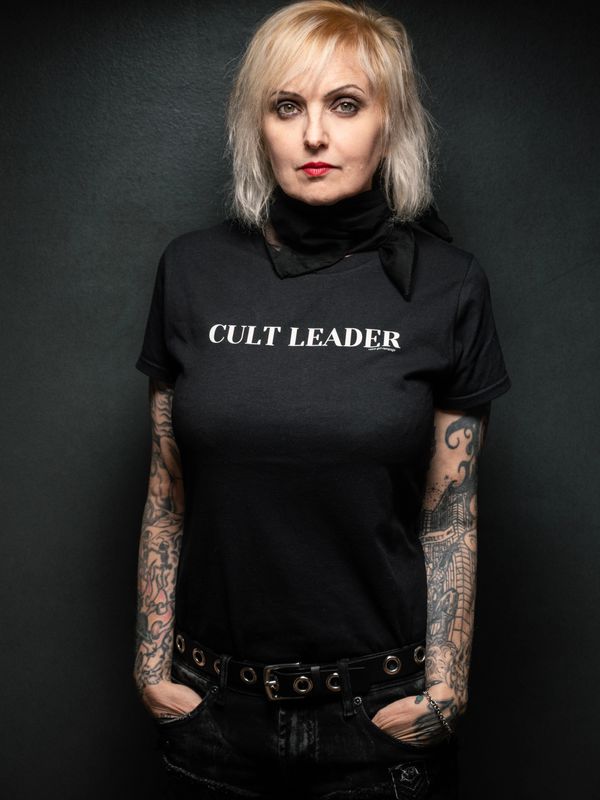 Woman wearing a "CULT LEADER" T-shirt with tattoos on her arms.