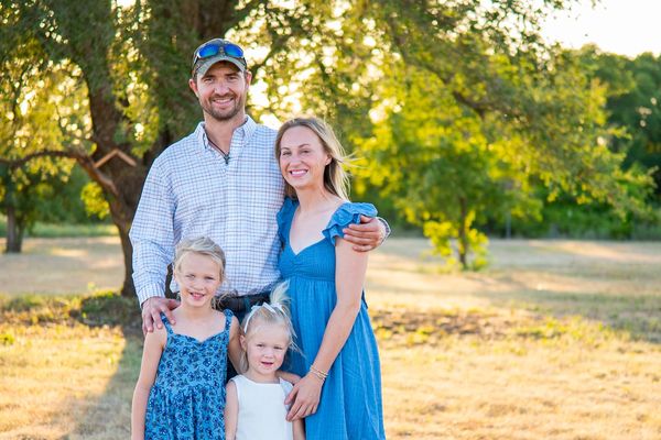 Smiling family of four posing outdoors in a sunny park.