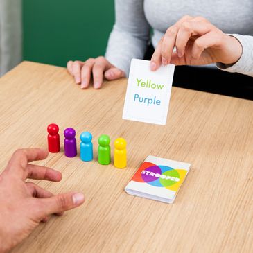 2 people playing, 5 coloured pawns lined up with the cards next to them, one card being turned over.